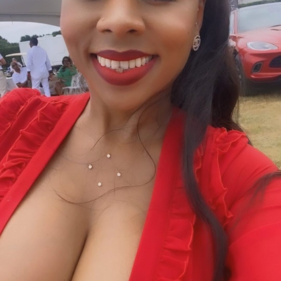 Woman smiling in a red dress at an outdoor event.
